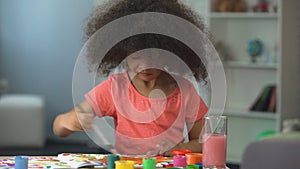 Cute African American girl painting a picture and smiling into camera, childhood