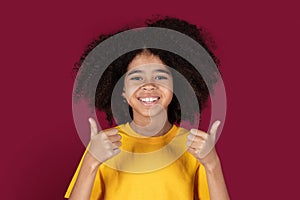 Cute african american girl showing thumb ups, isolated on burgundy
