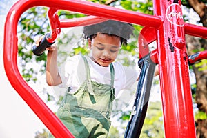 Cute African American little kid boy funny while playing on the Exercise machine in the daytime in the spring season. Outdoor