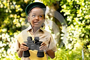 Cute african american scout girl in uniform holding binoculars in forest