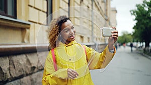 Cute African American teenager is talking to friends online skyping using smartphone and looking at screen standing