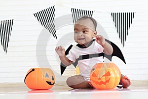 Cute African baby kid dressing up vampire fancy Halloween costume with black bat wings, cheerful little cute child holds Halloween