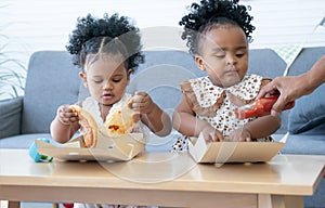 Cute African daughter eating pizza at home. Children kids enjoy and having fun with tasty lunch meal together. Parent help little