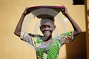 Cute African Girl Carrying a Couloured Handmade Straw Basket On Her Head