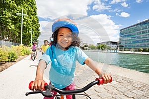 Cute African girl cycling along river embankment