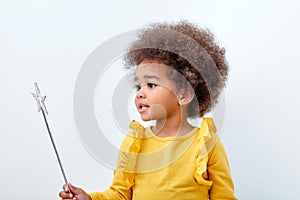 Cute african girl holding magic wand, white studio wall, copy space
