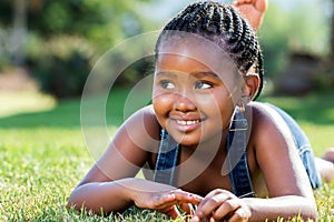 Cute african girl laying on green grass.
