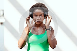 Cute African girl listening to music with headphones on the street and smiling