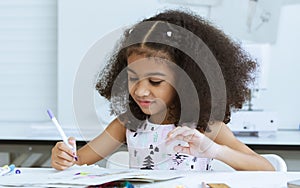 Cute African little girl drawing or sketching clothing design on paper at tailor room, cozy home as her career dream, smiling with