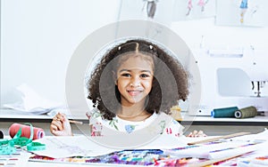 Cute African little girl drawing or sketching clothing design on paper at tailor room, cozy home as her career dream, smiling with