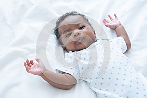 Cute African Nigerian newborn baby lying on white bed. Innocence 2 months infant wear clothes with curly hair looking at camera.