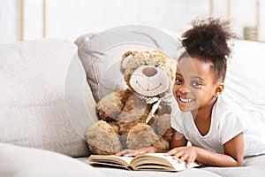 Cute afro baby girl playing with teddy bear, reading book