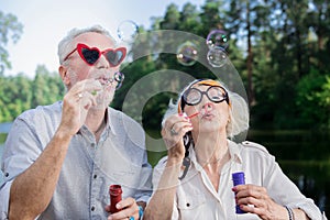 Cute aged couple wearing funny glasses and blowing soap bubbles