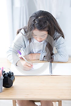 Cute Asia girl writing something in paper with colour pencils