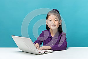 Cute asia little girl who enjoy the laptop computer on blue background