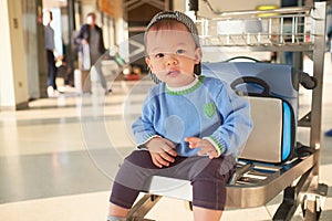 Cute Asian 2 years old toddler boy child with suitcase, sitting on trolley at airport, Family travel & vacation with kid concept