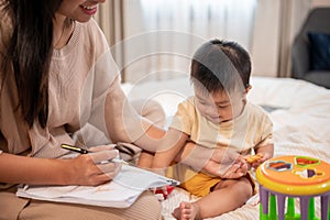 A cute Asian baby boy is trying to play and bothering his mom while she is working at home