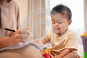 A cute Asian baby boy is trying to play and bothering his mom while she is working at home