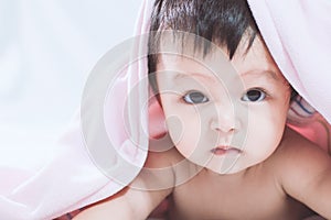 Cute asian baby girl smiling under pink blanket