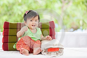 Cute asian baby girl in Thai traditon dress sitting with pillow