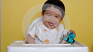 Cute asian baby sits on highchair and smiling on yellow background