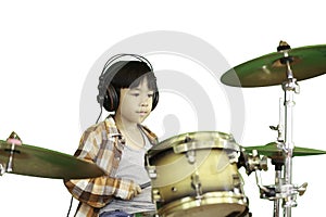 A cute Asian boy is enjoying playing the drums in a music classroom.