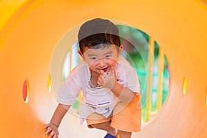 Cute Asian boy playing and smiling in yellow tunnel at the playground with sunlight yellow tube,