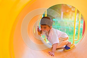 Cute Asian boy playing and smiling in yellow tunnel at the playground with sunlight yellow tube,