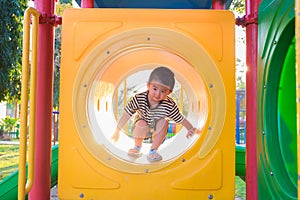 Cute Asian boy playing and smiling in yellow tunnel at the playground with sunlight yellow tube,