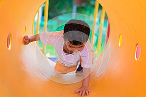 Cute Asian boy playing and smiling in yellow tunnel at the playground with sunlight yellow tube,