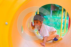 Cute Asian boy playing and smiling in yellow tunnel at the playground with sunlight yellow tube,