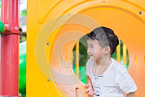 Cute Asian boy playing and smiling in yellow tunnel at the playground with sunlight yellow tube,