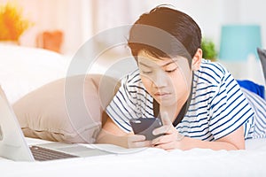 Cute asian boy rest on bed and using smart cell phone with smile