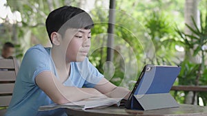 Cute asian boy using tablet computer, young teenage boy doing homework on digital tablet with silently face .