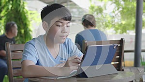 Cute asian boy using tablet computer, young teenage boy doing homework on digital tablet with silently face .