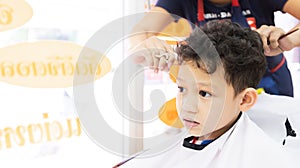 Cute asian child boy getting hair cut by hairdresser at hair salon.