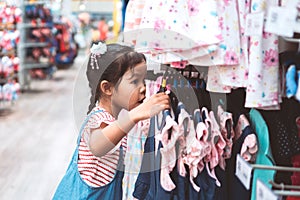 Cute asian child girl choosing dresses in clothes department