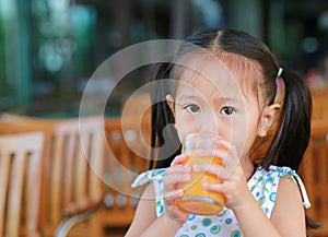 Cute asian child girl drinking Orange juice at restaurant with looking camera