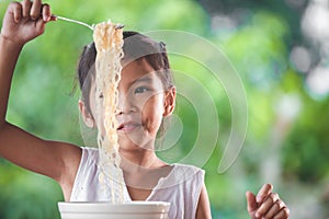 Cute asian child girl eating delicious instant noodles with fork