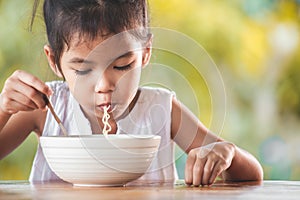 Cute asian child girl eating delicious instant noodles with fork