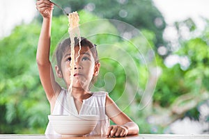 Cute asian child girl eating delicious instant noodles with fork