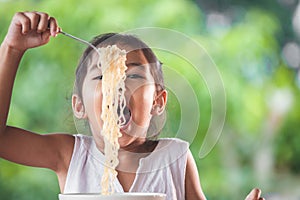 Cute asian child girl eating delicious instant noodles with fork