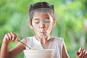 Cute asian child girl eating delicious instant noodles with fork