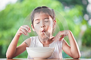 Cute asian child girl eating delicious instant noodles with fork