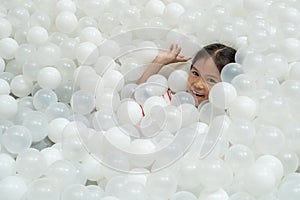 Cute asian child girl having fun to play with white plastic balls in the playground
