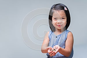 Cute Asian child girl holding coins in her hands. Sweet smiling kid. Happy children playing silver coins. Baby looking at camera.