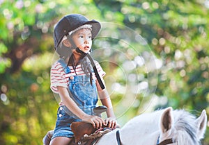 Cute asian child girl riding a horse in the farm