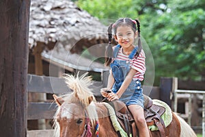 Cute asian child girl riding a pony in the farm