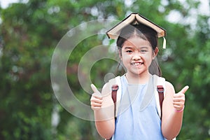 Cute asian child girl with school bag put a book on head