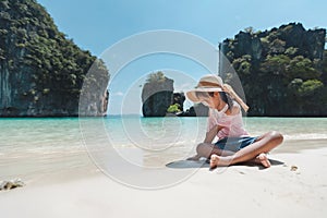 Cute asian child girl wearing hat and sunglasses sitting on the beach and playing with sand. She is enjoying with beautiful nature